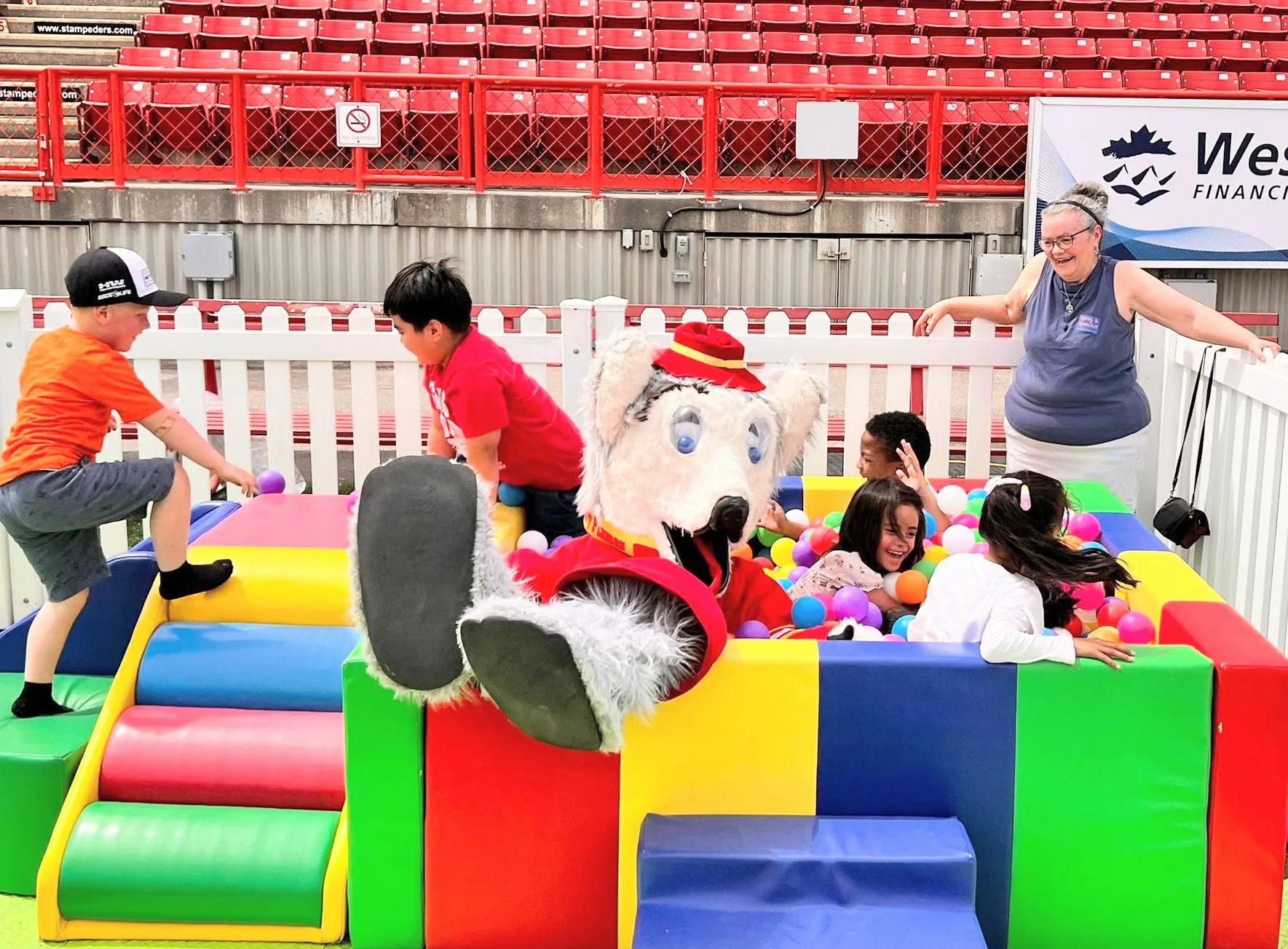 Kids enjoy a colorful ball pit with a mascot figure wearing a red hat.