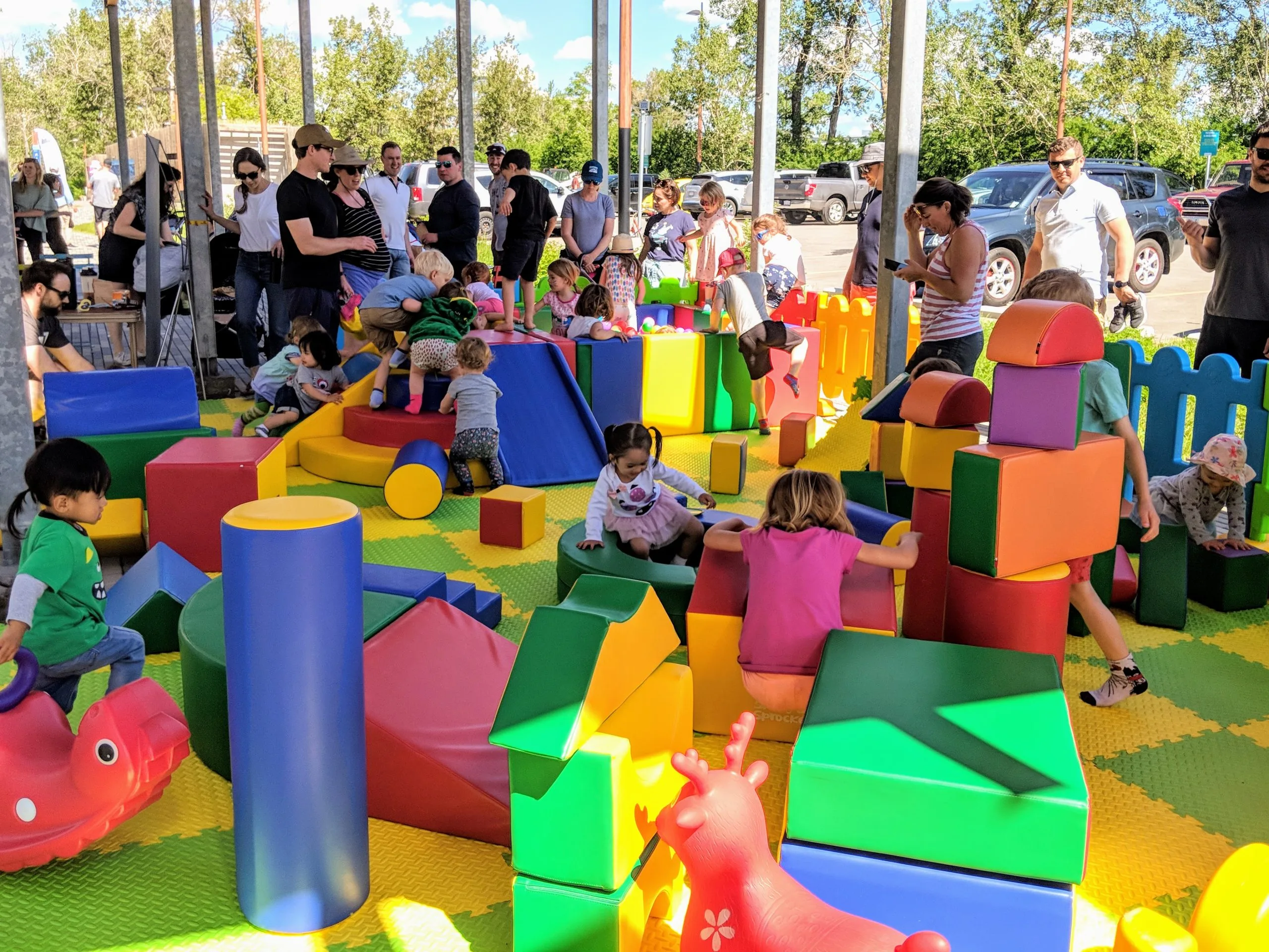 Kids and adults at a vibrant outdoor playground with large foam blocks and toys.