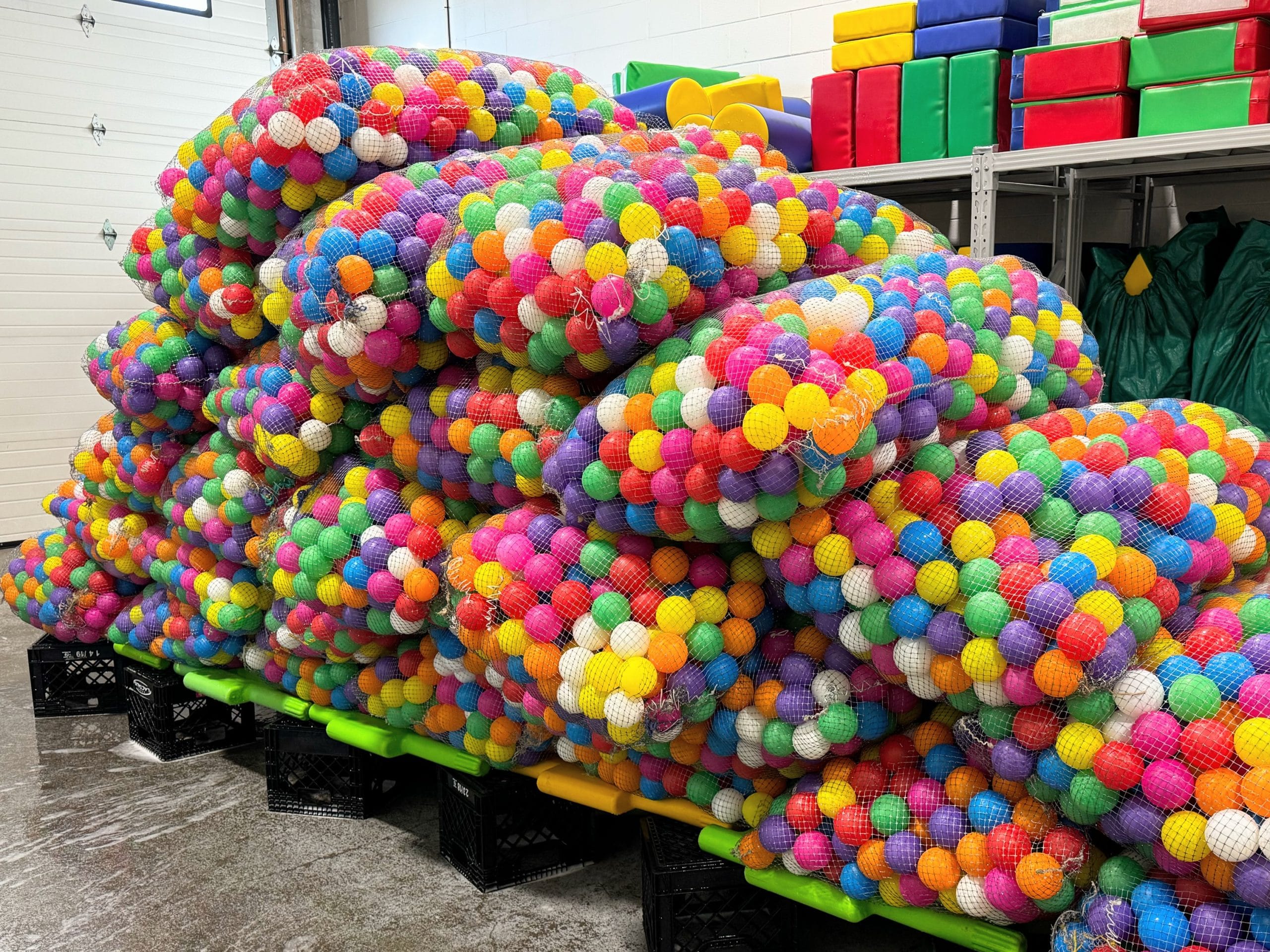 Large bags filled with colorful plastic balls stacked on shelves in a storage room.