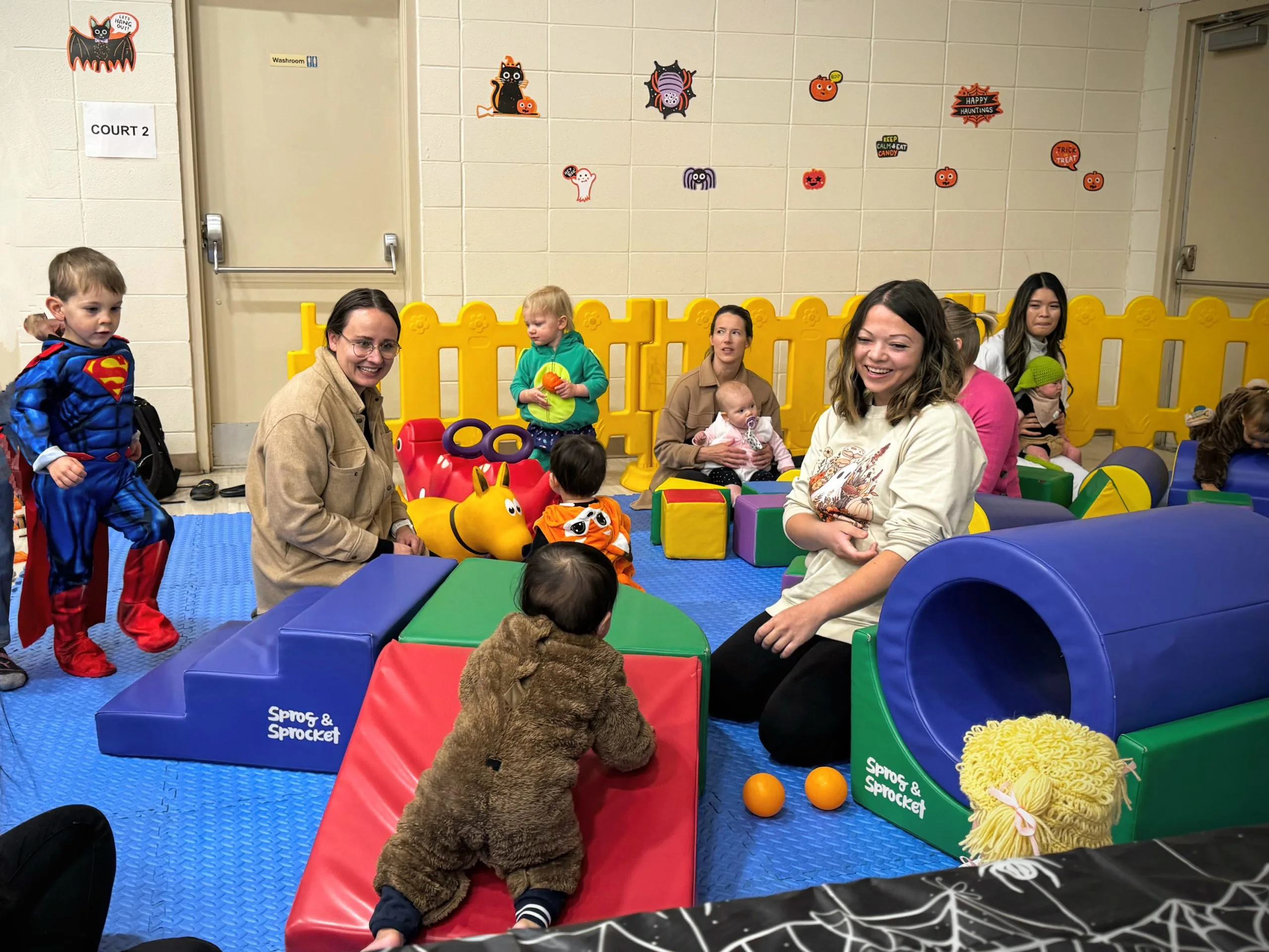 Children and adults in costumes enjoying a colorful indoor play area with props.